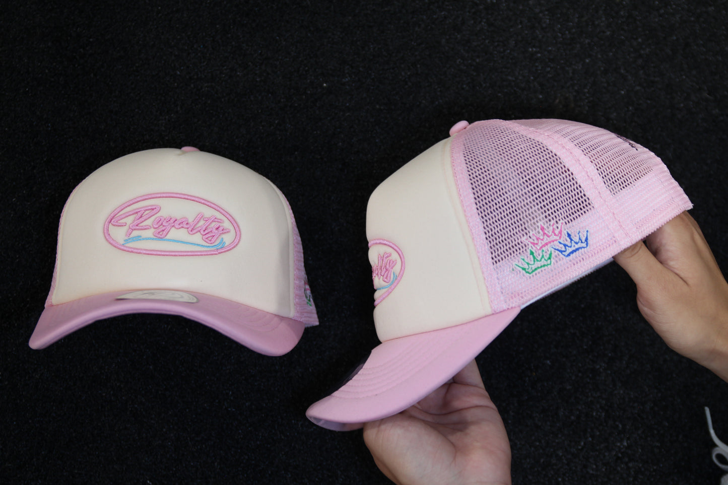 Two pink caps with embroidered designs on a black background
