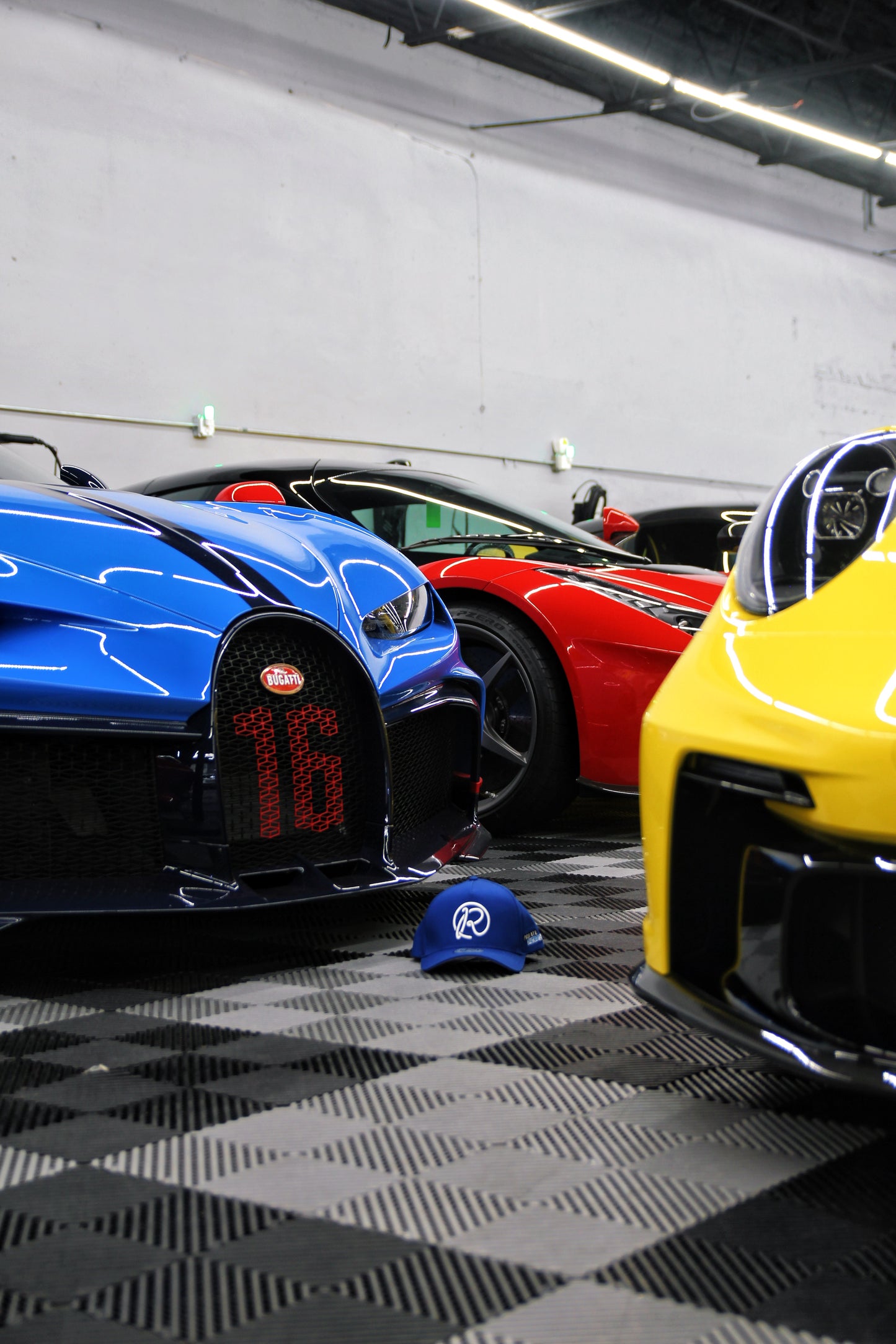 Three high-end sports cars parked in a garage with a cap on the floor.