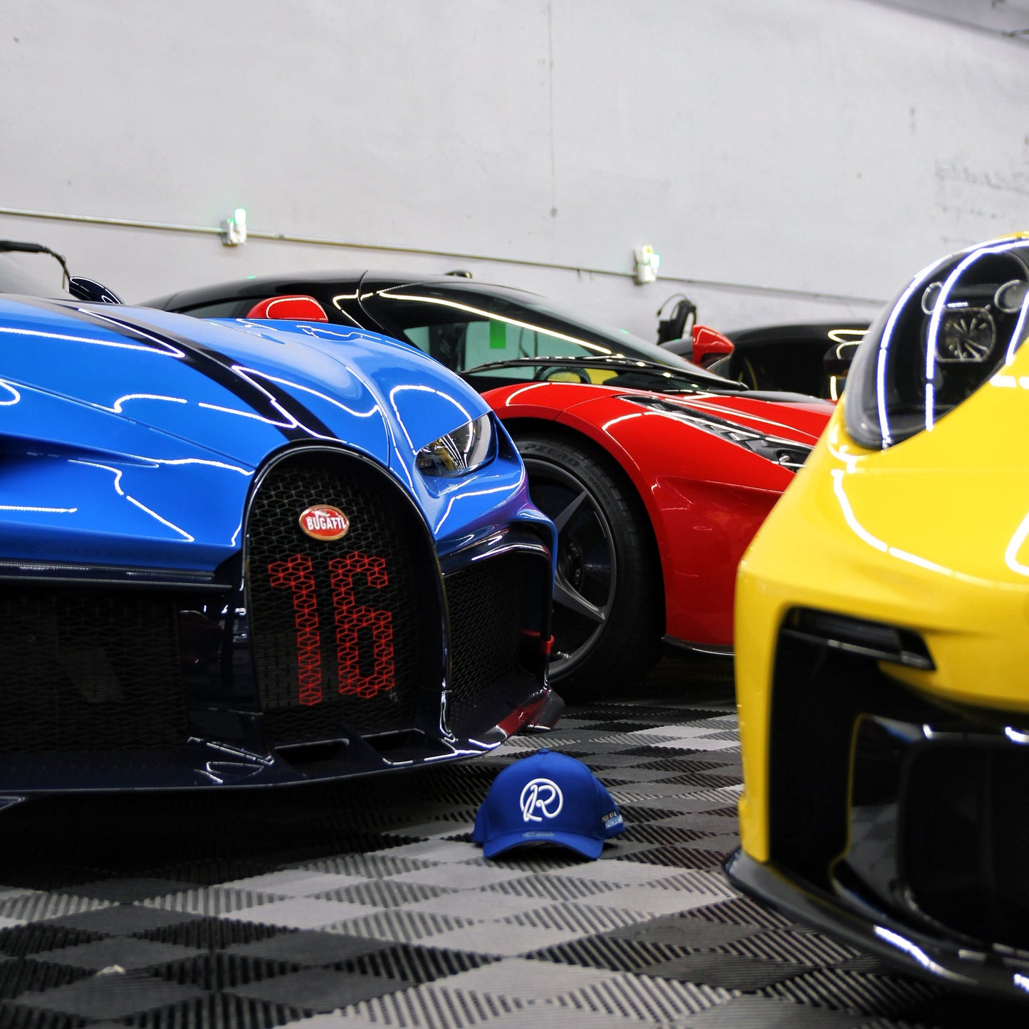 Three high-end sports cars parked in a garage with a cap on the floor.