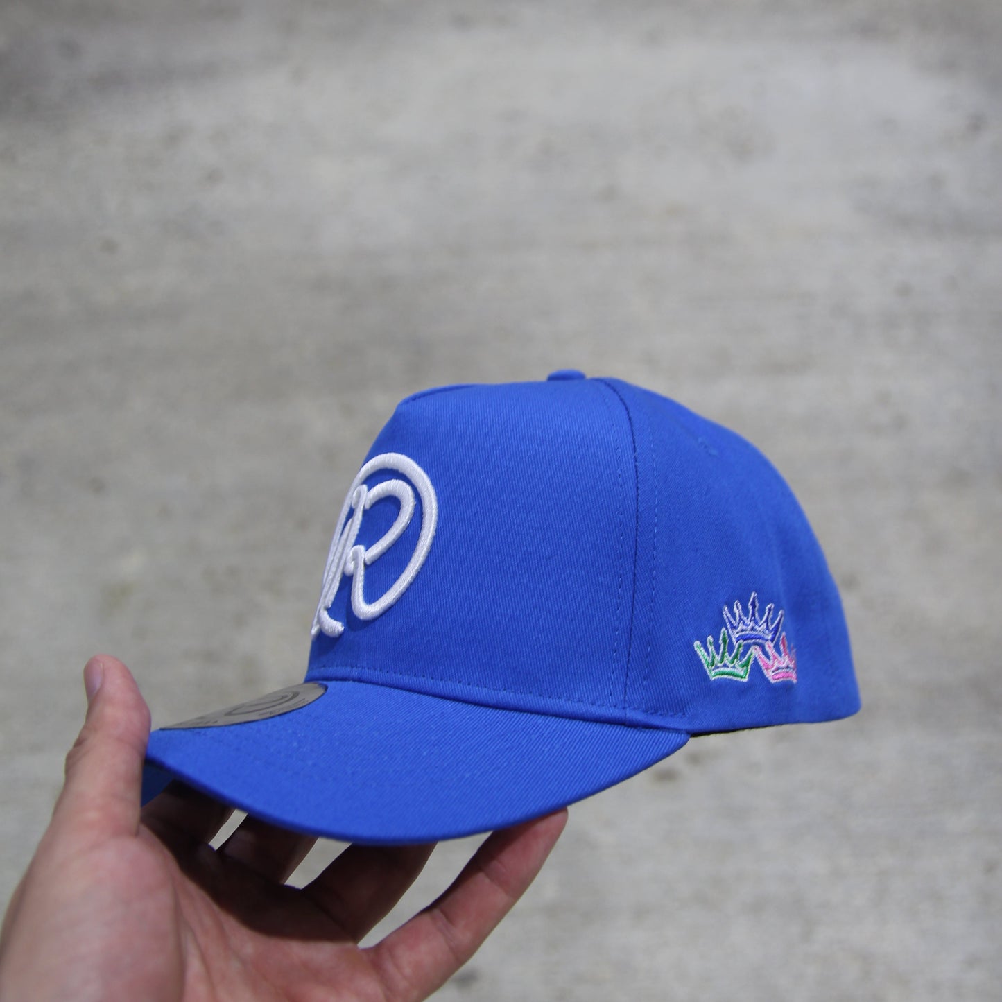 Blue cap with white logo held by a hand on a gray background