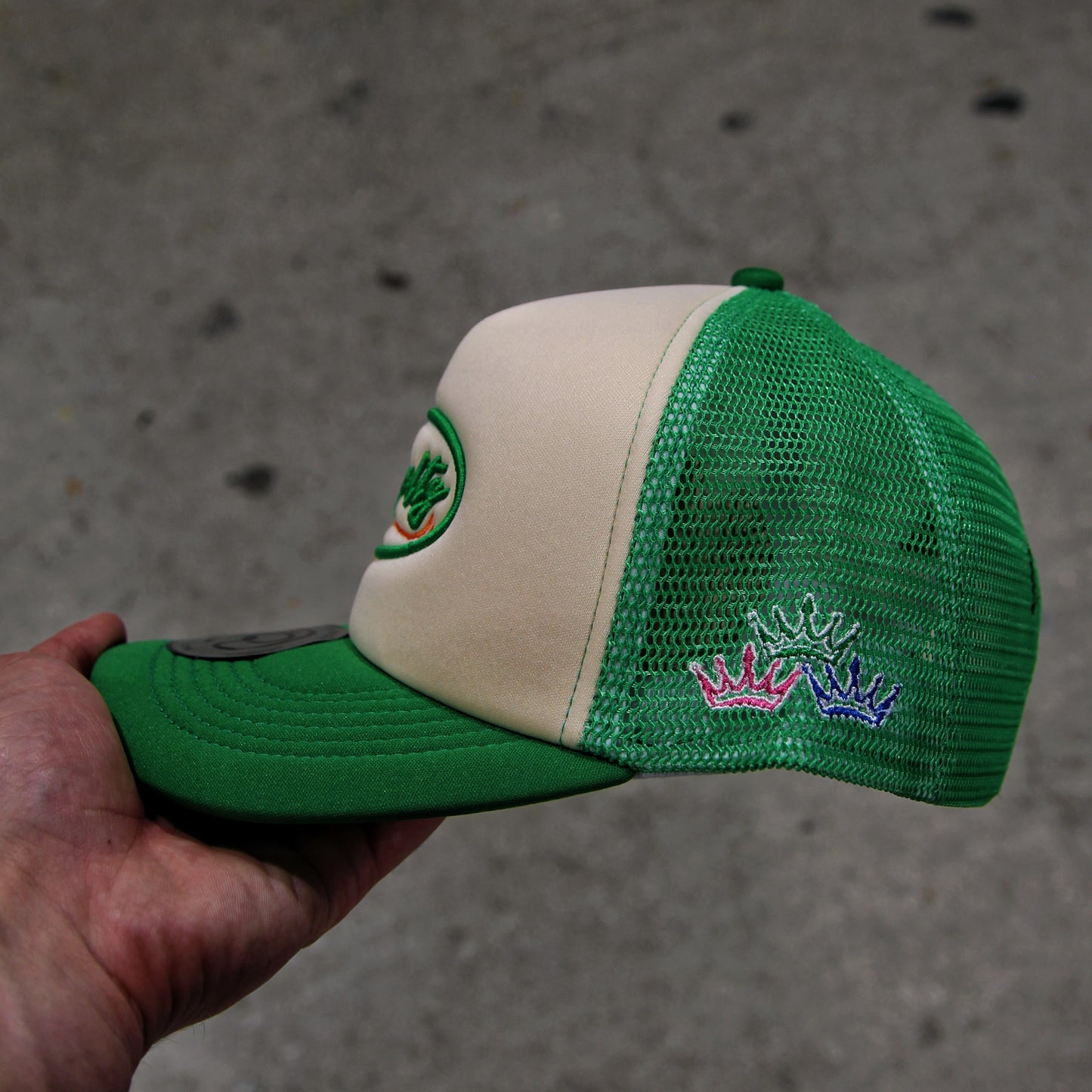 Green and beige cap with embroidered designs held against a gray background