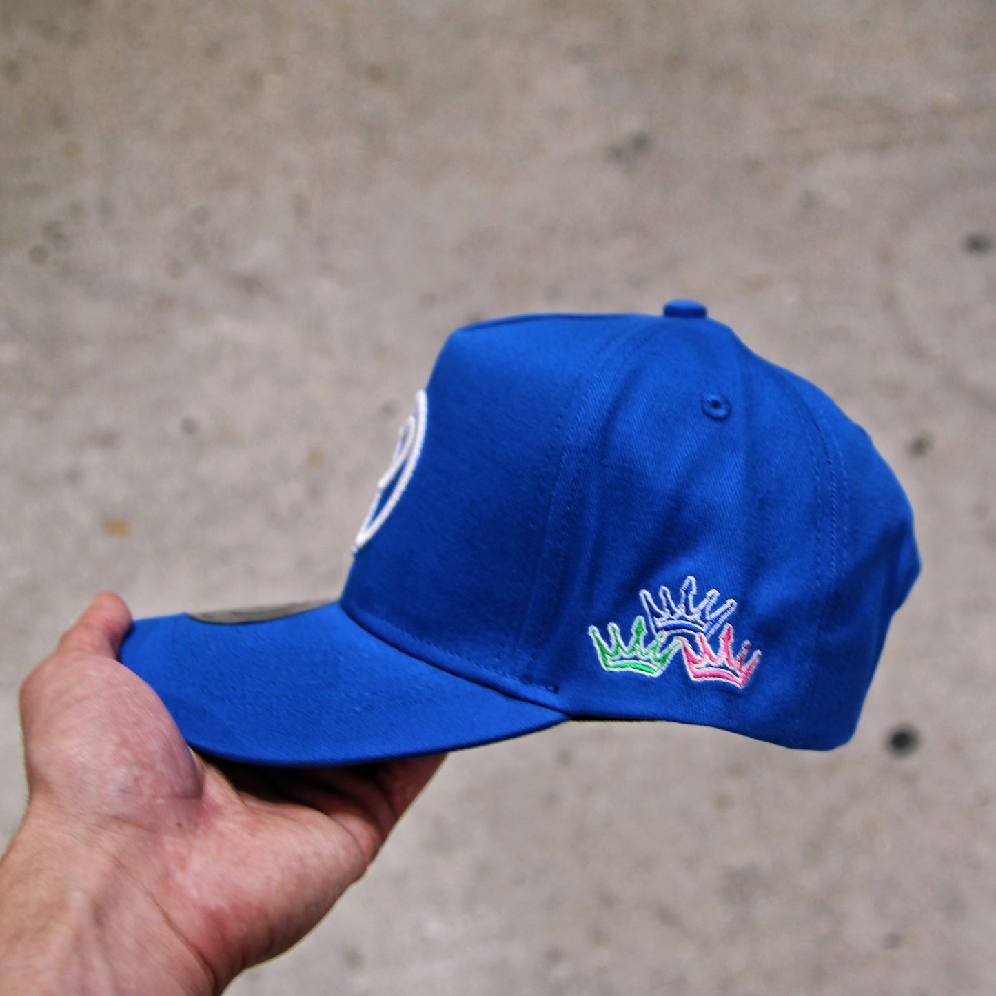 Blue cap with a logo held by a hand against a concrete background