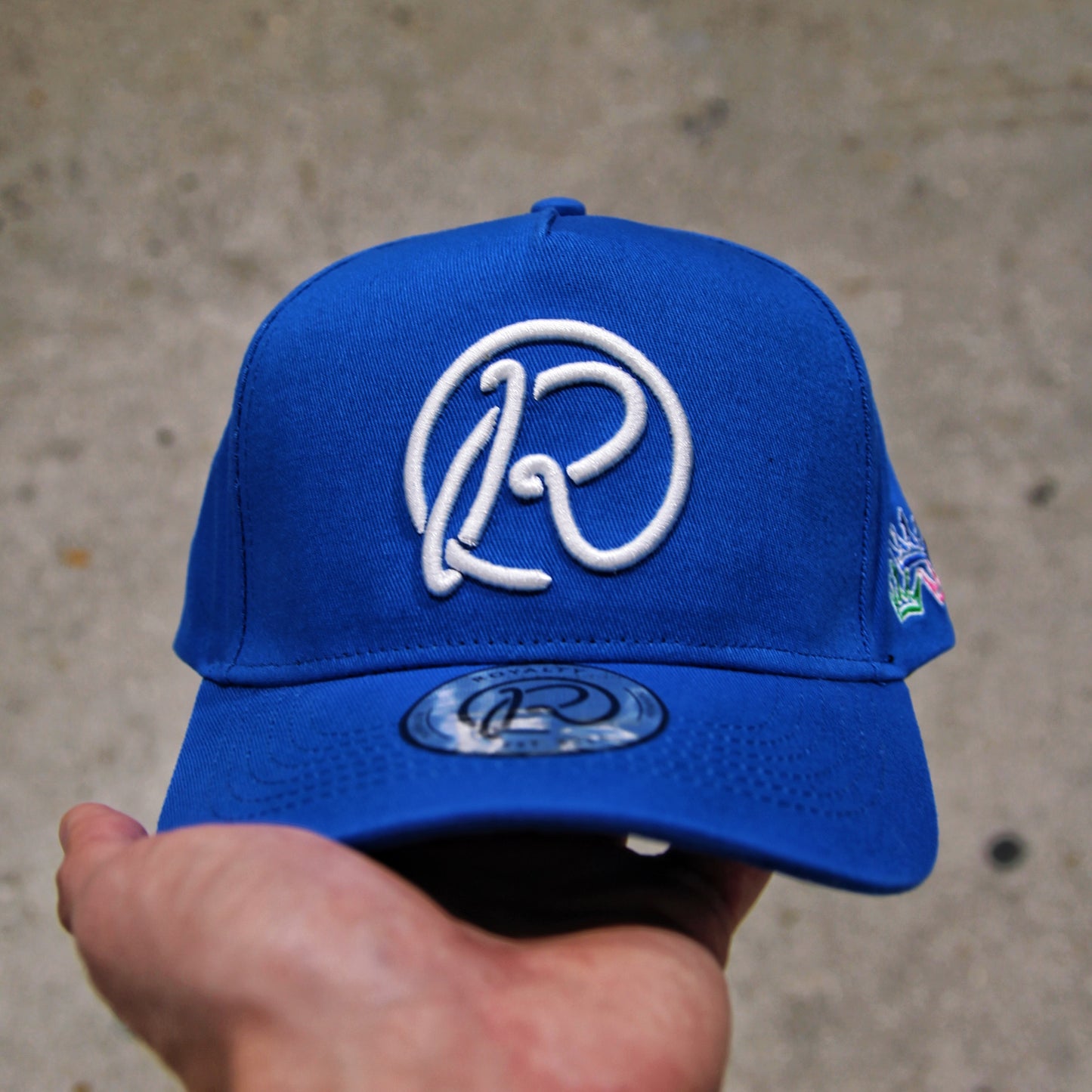 Blue cap with a white logo held by a hand against a concrete background