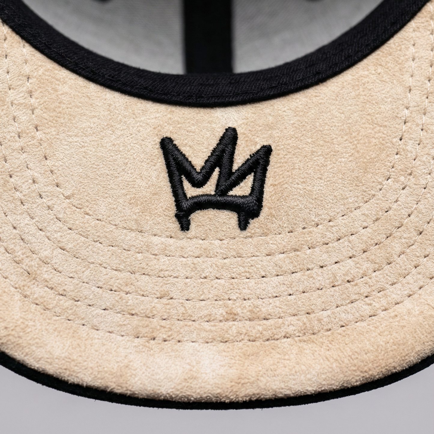 Close-up of a beige cap with a black embroidered logo on a gray background