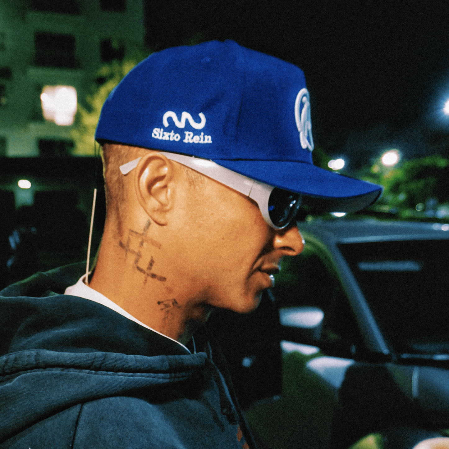 Person wearing a blue cap with branding, standing outdoors at night.
