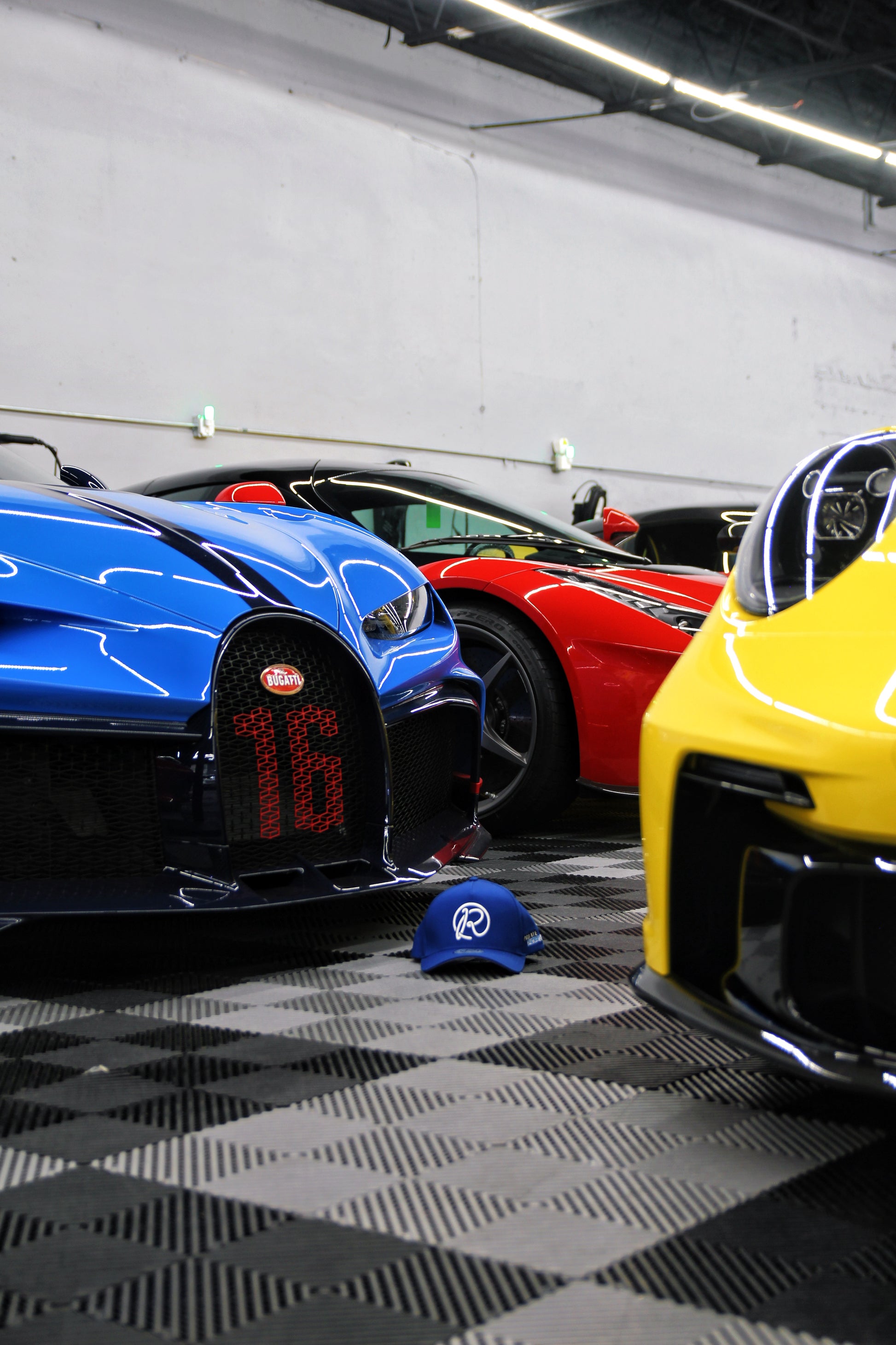 Three high-end sports cars parked in a garage with a cap on the floor.
