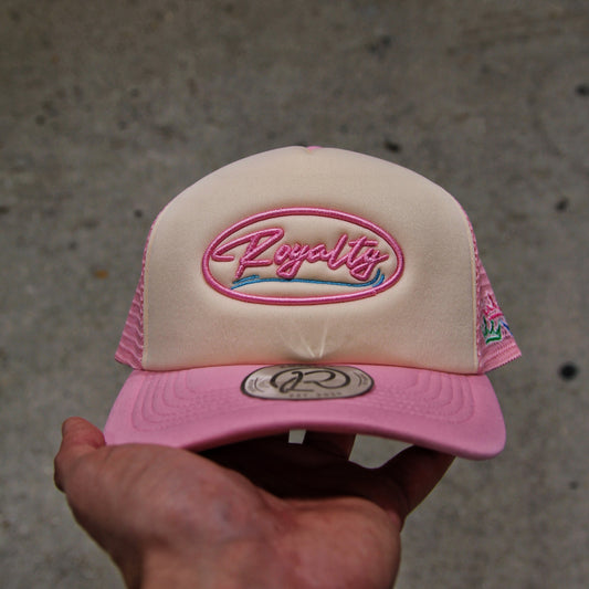 Pink and beige cap with 'Royalty' logo held by a hand on a concrete surface
