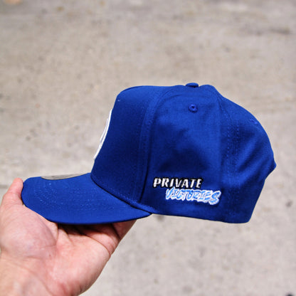 Blue cap with 'PRIVATE VICTORIES'  text held by a hand on a concrete surface