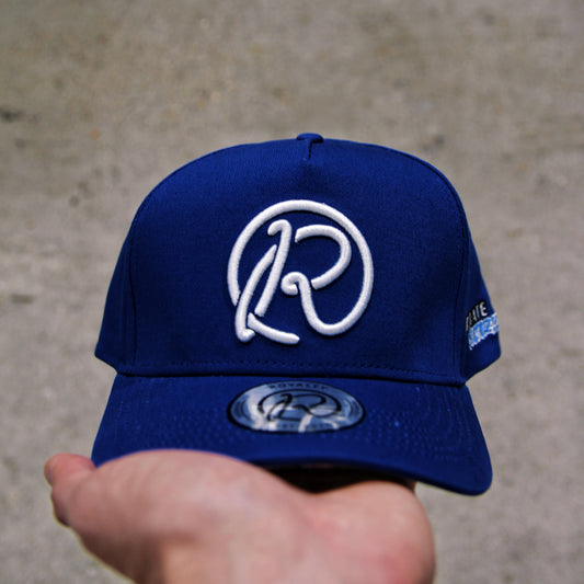 Blue cap with a white logo held by a hand against a concrete background